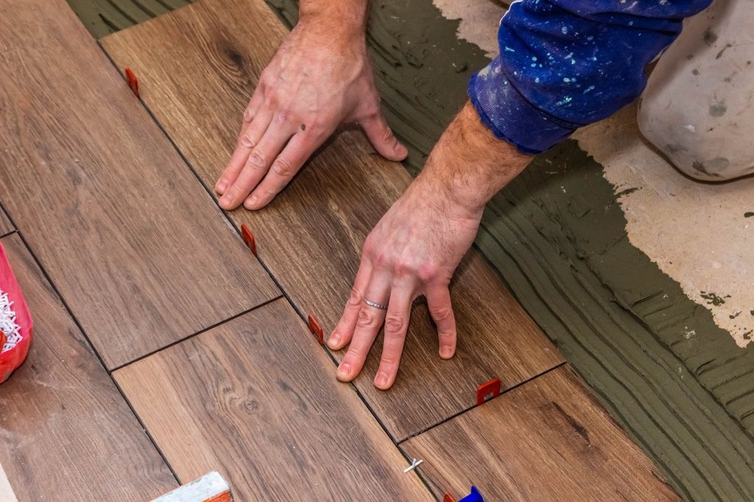 Händer som installerar golvplattor med träutseende och röda kakelkryss.